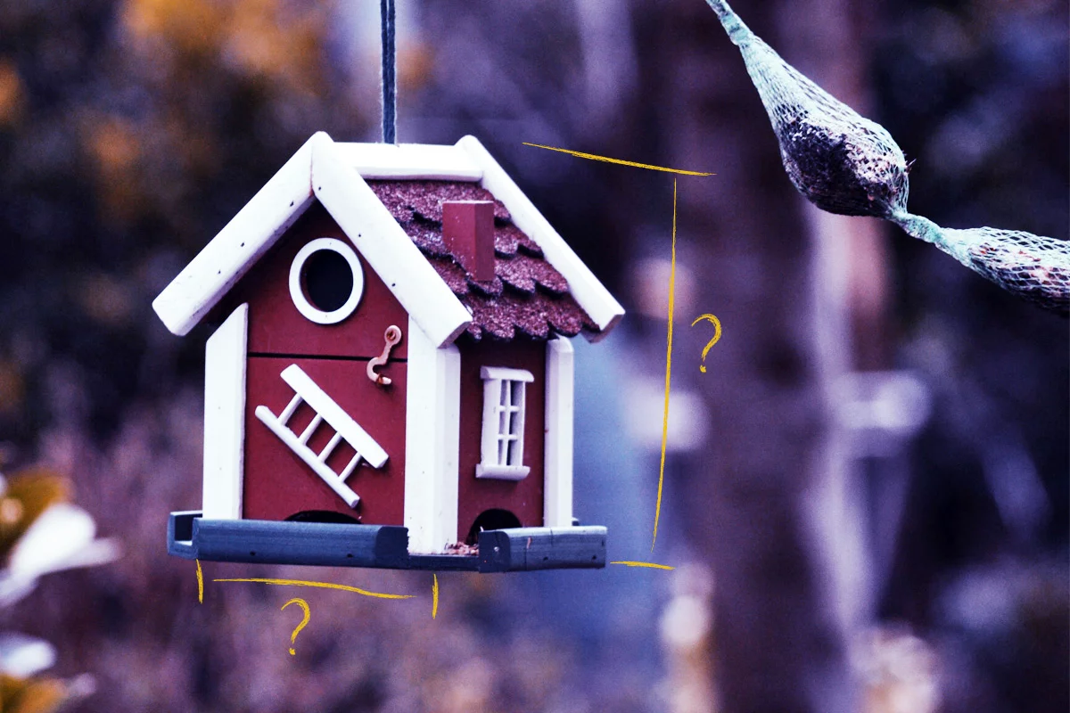 A close-up of a small, red birdhouse with white trim, hanging outdoors. The charming garden building features a ladder and various painted details. Surrounding the birdhouse is a measurement-like overlay with question marks, suggesting curiosity about its dimensions. - a room in the garden