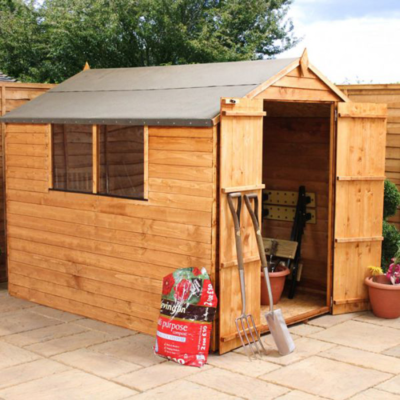 A wooden garden shed with an open door is situated on a paved area with a wooden fence in the background. The shed, envisioned as a potential garden office, has two windows on one side. Gardening tools, a wheelbarrow, and a bag of compost are placed near the entrance. There are potted plants nearby. - a room in the garden