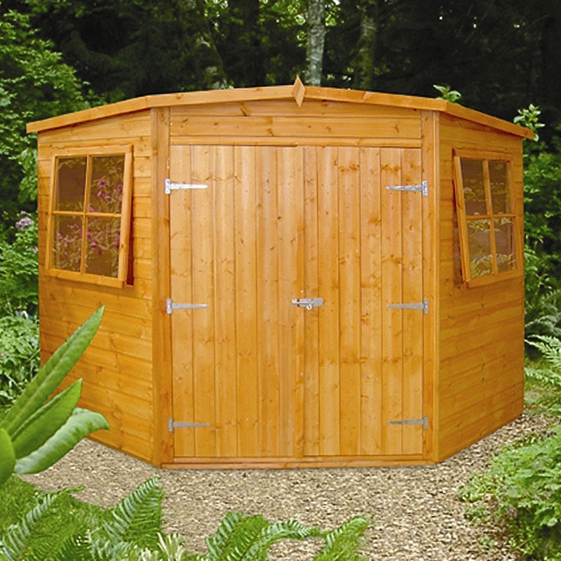 A wooden garden shed with a pentagonal shape, featuring double doors secured with a latch and two windows on either side, serves as a cozy garden office. Situated on a gravel path and surrounded by a lush, green garden with ferns and various plants, it’s an ideal workspace retreat. - a room in the garden