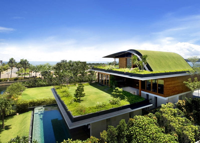 A modern house with a unique green roof covered in grass and plants. The property features an expansive lawn, lush landscaping, and an outdoor pool. The architectural design seamlessly blends elements of nature, making the home's architecture harmonize perfectly with its surroundings. - a room in the garden