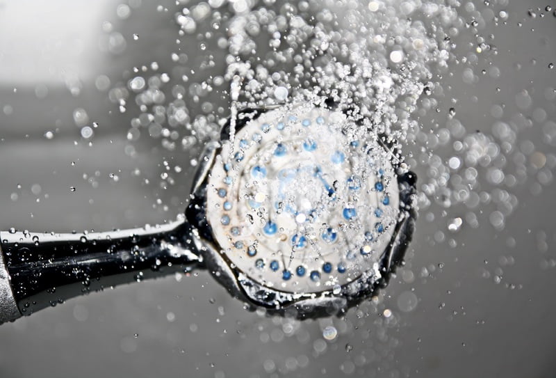 A close-up image of a showerhead spraying water. The showerhead features multiple small, round nozzles and is discharging a stream of water droplets. The background is blurred, emphasizing the focus on the water spray and showerhead—an inspiration to connect water to my garden room. - a room in the garden