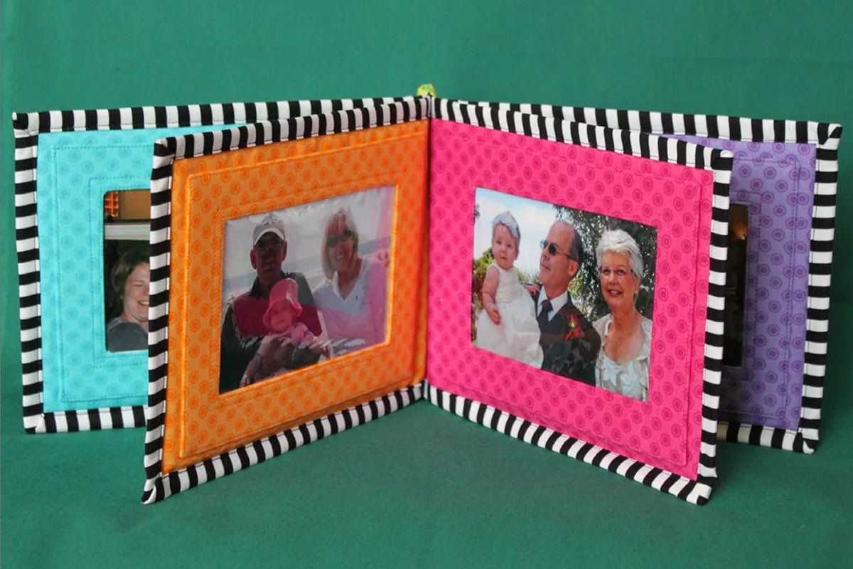 A colorful photo album with black and white striped borders is opened to display four framed pictures on a green background, reminiscent of serene garden baby room ideas. The frames are in blue, orange, pink, and purple colors, showcasing various family and individual photos. - a room in the garden