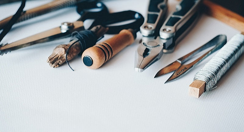 A collection of various woodworking tools, including a pair of scissors, a wooden-handled tool, pliers, and a metal file, are arranged on a white surface. Some tools have handles wrapped in string or wire, perfect for crafting custom features in garden rooms. - a room in the garden