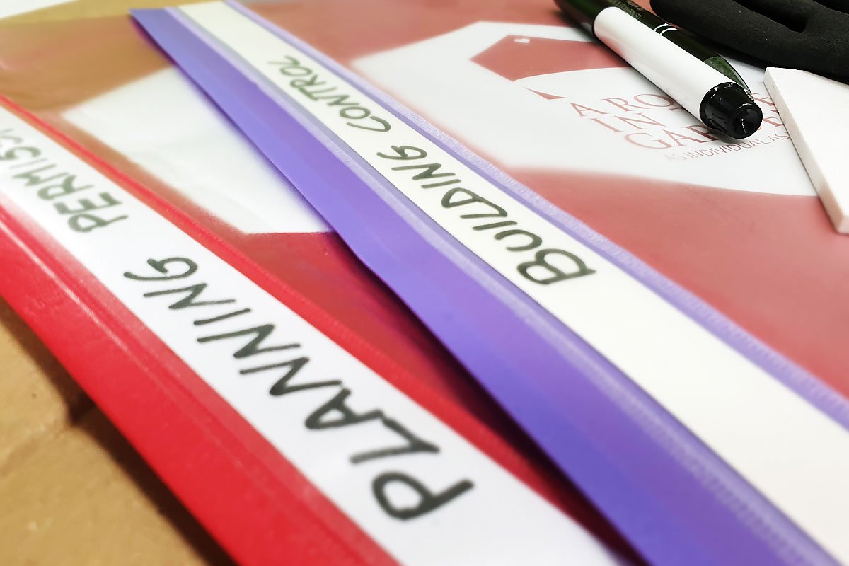 A close-up image of three organized binders on a desk, labeled "Planning Permission," "Building Control," and "A Room in the Garden." A white pen and some papers related to planning permission are visible in the background. - a room in the garden