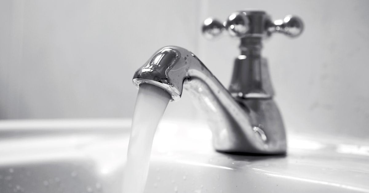 A close-up of a chrome faucet with running water in a sink. The background is slightly blurred, emphasizing the shiny faucet and the smooth flow of water into the white basin. The faucet has a rounded handle on top for adjusting water flow, reflecting its cost-effective design. - a room in the garden