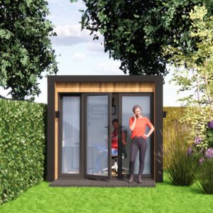 A woman in a red shirt stands talking on the phone outside a small modern garden office with large glass doors. Inside, a man sits at a desk looking at a computer. The office is surrounded by lush greenery and trees. - a room in the garden