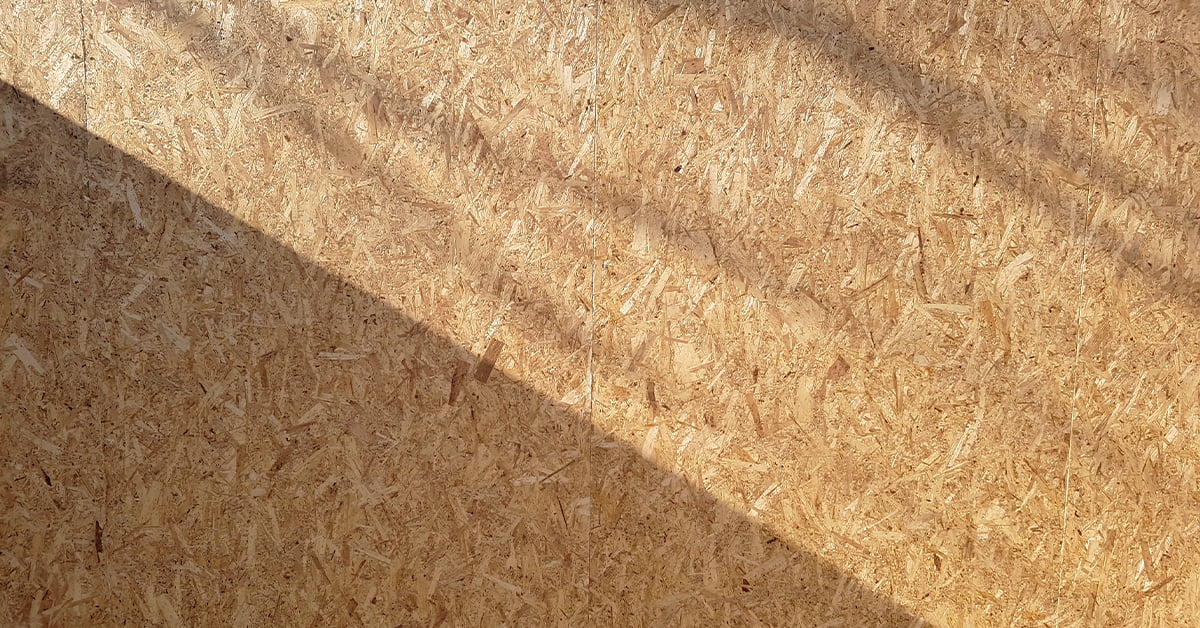 A close-up of an oriented strand board (OSB) surface, akin to that used in SIP panels, illuminated by sunlight. The wood particles are visible, creating a textured pattern. Diagonal shadows are cast on the board, creating contrast and highlighting the texture. - a room in the garden