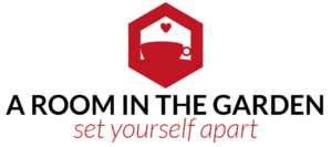Logo for "A Room in the Garden" featuring a red hexagon with a silhouette of a room inside, including a table, chair, and heart above them. The text below reads "A Room in the Garden" in black and "set yourself apart" in red. - a room in the garden