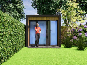 A woman in a red shirt and black pants stands in front of a modern, small garden office with glass doors. She is talking on her phone, with lush green grass, hedges, and colorful flowers surrounding the office. Tall trees rise in the background. - a room in the garden